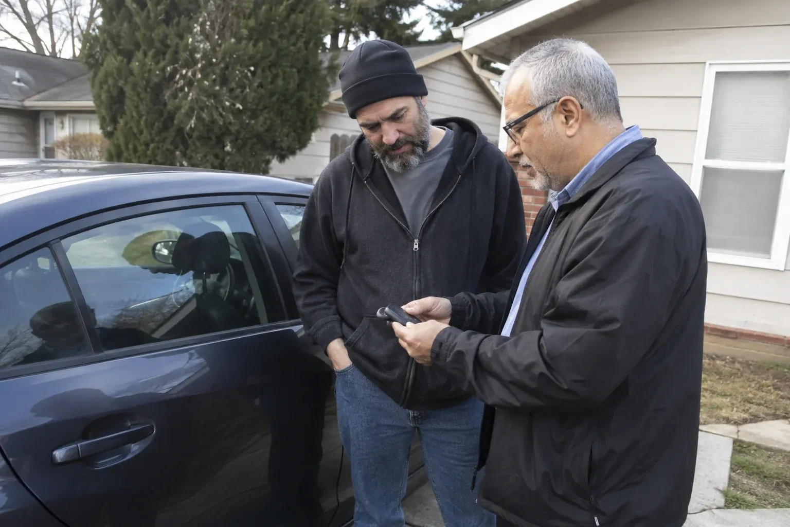 Two adults discussing a key fob beside a parked car. — Car Lockout Service, Hamilton