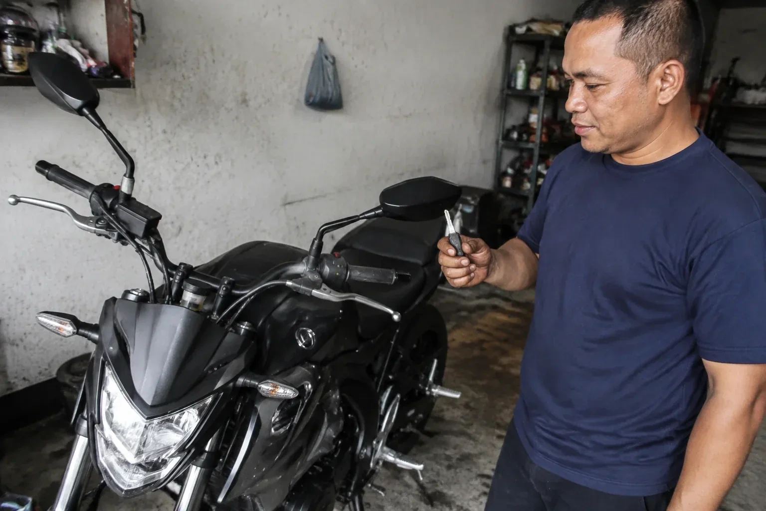 Person holding a key beside a black motorcycle in a garage. — Motorcycle & Scooter Keys, Hamilton