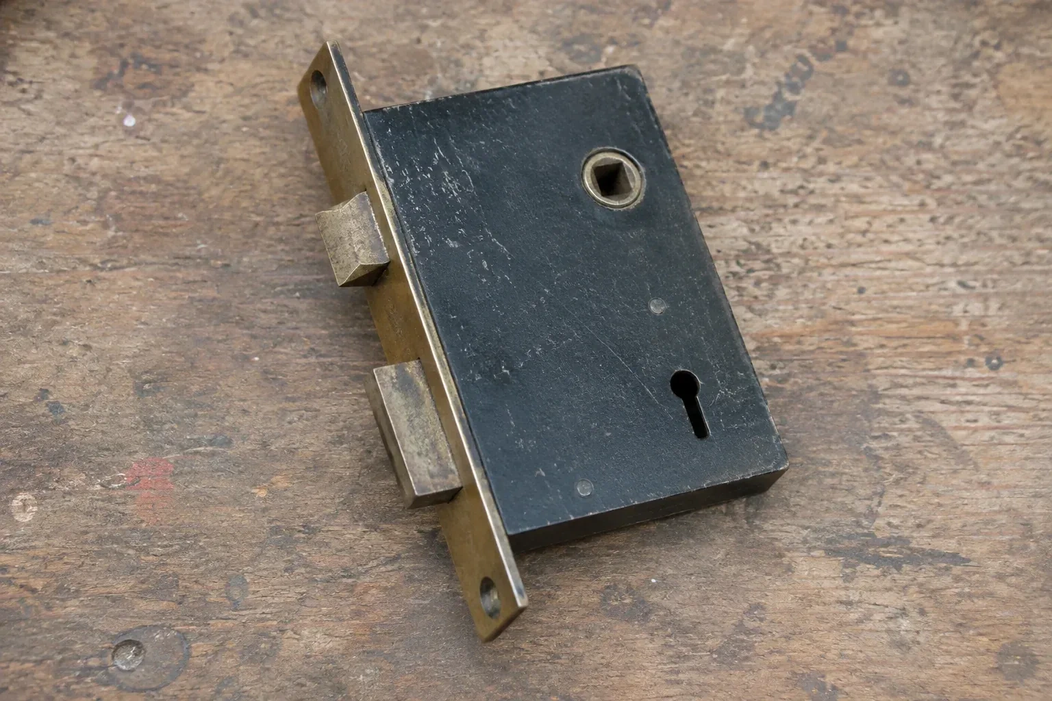 Closed mortise lock case with spindle opening, keyhole, latch and deadbolt on a wooden workbench. — Vintage Mortise Lock Service, Maple Lane Annex
