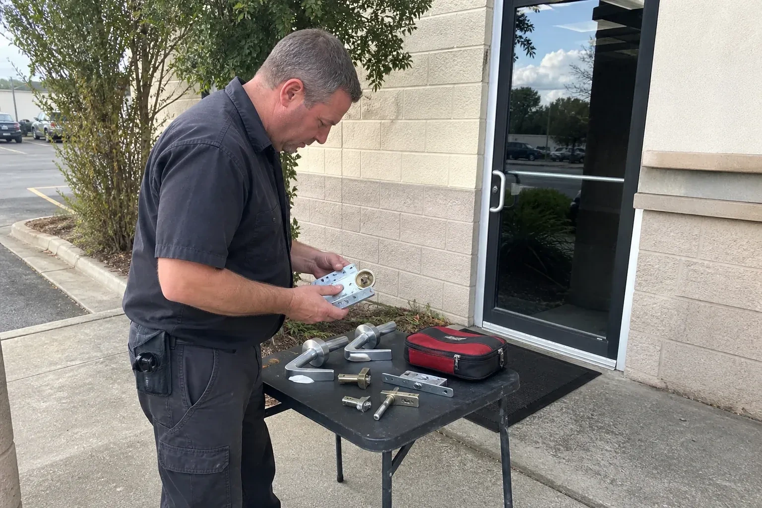 Technician examining detached commercial lock hardware on a table outside a shop entrance. — Business Lockout Service, Hamilton
